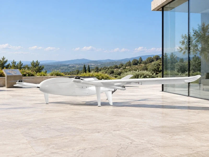 UG25 in its approved three-quarter view on a spacious pale stone terrace beside a tall glass wall, distant vegetation and a separate date-free site plan stand