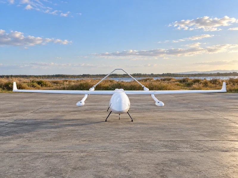 UG62 head-on with the exact approved wing, inverted-V tail and undercarriage, stationary on a wide empty environmental field-station apron beside distant reed beds.