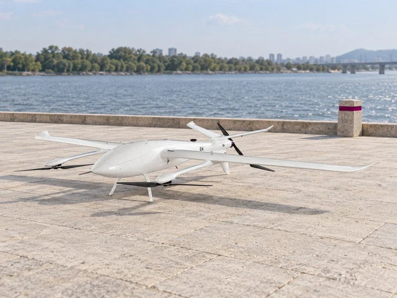 UG39 in its approved oblique orientation resting on an empty pale stone riverside terrace with distant water and a separate magenta marker