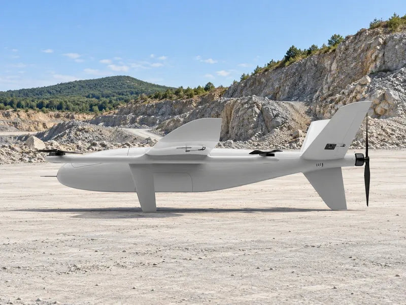 UG35 in its exact approved left-facing side profile resting on a broad outdoor pale concrete field-engineering pad beside an open gray rock quarry, distant low green ridge and clear sky, no cases, tools, benches or buildings.
