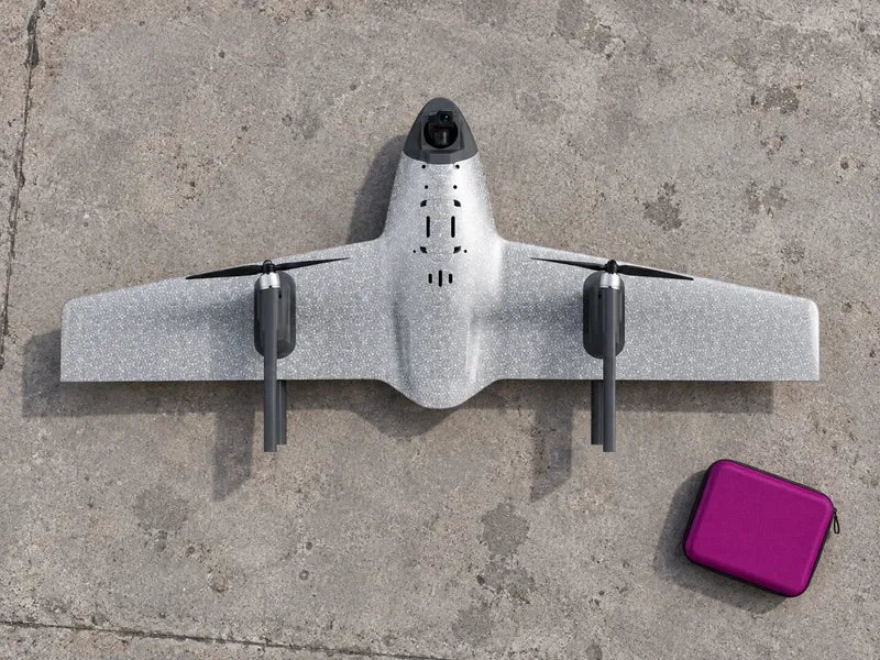 UVH1 stationary on an empty gray survey staging slab beside a closed magenta field folio, viewed from above, complete wings visible